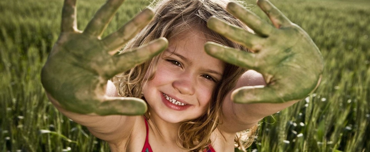 Ein kleines Mädchen, welches grüne Farbe auf ihren Handflächen hat.